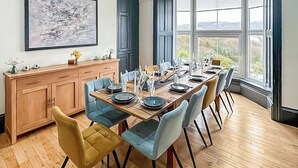 A dining area with a long table set for six, surrounded by six chairs, a wooden cabinet, and a large window with a view.