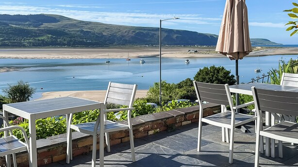 A seaside patio with outdoor seating and a view of the beach and boats.