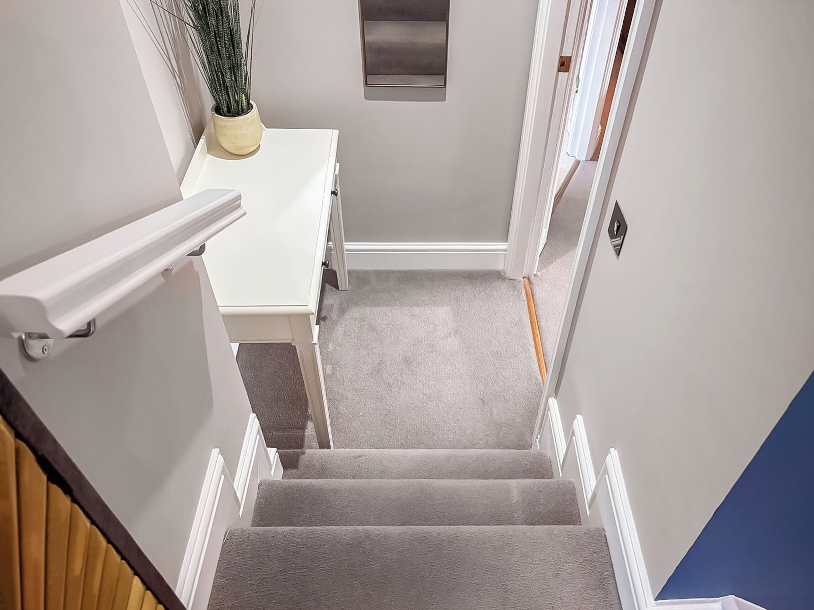 A staircase with a handrail, carpeted steps, a white wall, and a potted plant.