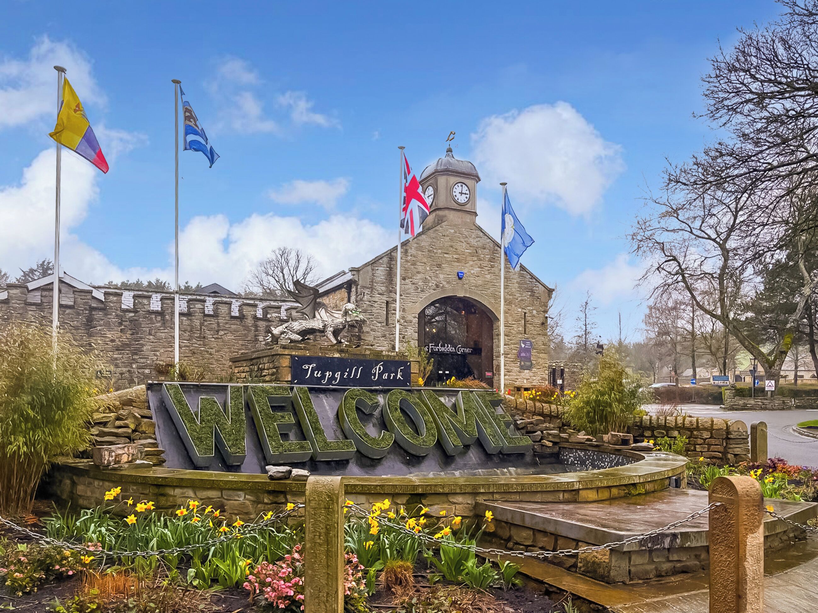 A stone building with a clock tower, a welcome sign, and flags.