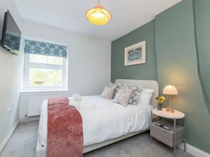 A bedroom with a bed, bedside table, lamp, and a window.