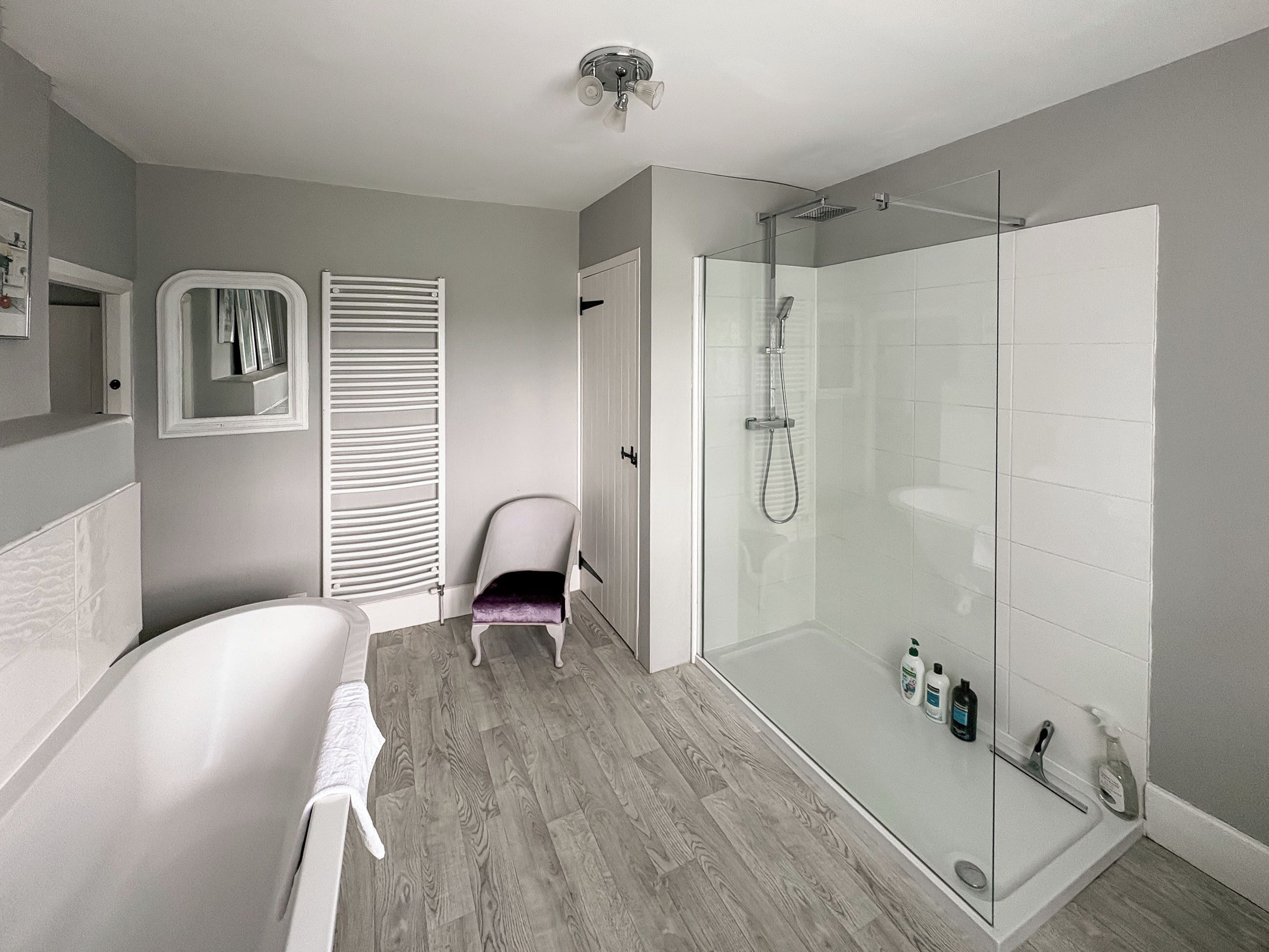 A modern bathroom with a glass-enclosed shower, a freestanding bathtub, and a chair.
