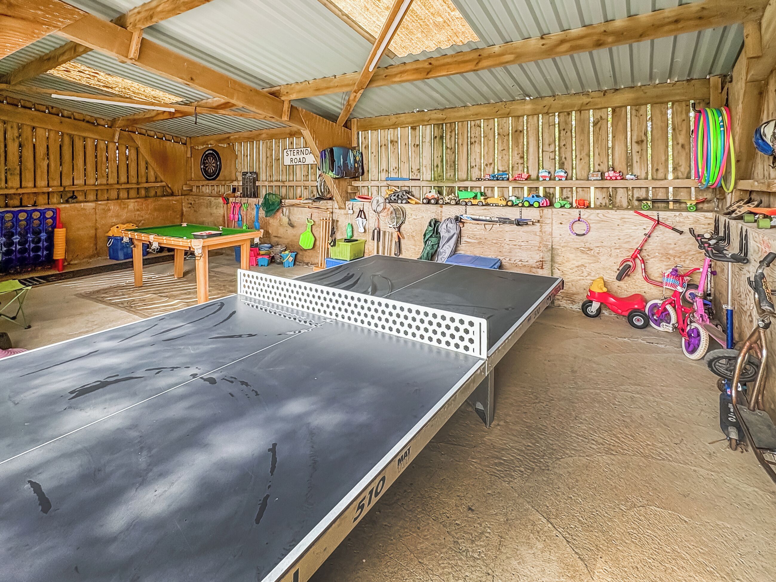 A ping pong table, a dartboard, and various toys in a rustic indoor space.