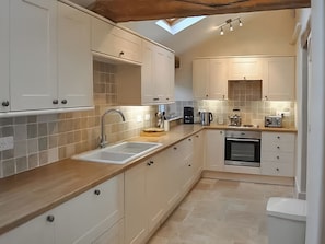 A modern kitchen with white cabinets, a wooden countertop, a skylight, and a built-in oven. - Lower Park Farmhouse (Lyme Regis)