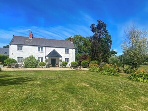 A white house with a dark roof, a front porch, and a garden with various plants and flowers. - Lower Park Farmhouse (Lyme Regis)