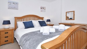 Een keurig opgemaakt bed met een houten hoofdbord, twee nachtkastjes met lampen, een klein nachtkastje met een schaal, en een spiegel aan de muur.