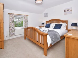 A bedroom with a wooden bed, two bedside tables, a window with floral curtains, and a view of greenery outside. - Set in the heart of Conwy Town, with views over the railway and Castle walls. (Conwy Town)