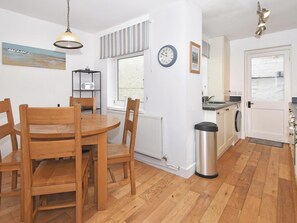 A kitchen with a dining table, chairs, a clock, a radiator, a trash bin, and a washing machine. - Set in the heart of Conwy Town, with views over the railway and Castle walls. (Conwy Town)