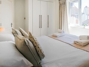 Ein Schlafzimmer mit Bett, Kissen, einem Fenster mit Vorhängen und Blick auf Gebäude.