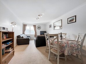 A cozy living room with a sofa, a dining table with chairs, a bookshelf, a TV, and a window with curtains. - Swallows Haven - UK51879 (Whitby)