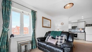 A living room with a black leather sofa, a small table, and a window with curtains. - Abbey Lights - UK51880 (Whitby)