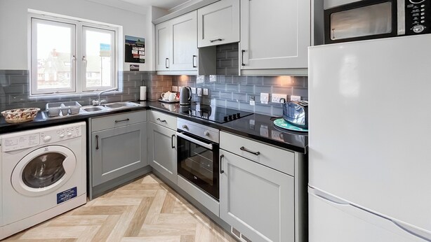 A modern kitchen with grey cabinets, a built-in oven, a microwave, and a washing machine. - Abbey Lights - UK51880 (Whitby)