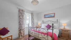A bedroom with a metal bed frame, a wooden chair, a bedside table with a lamp, and a window with curtains. - Abbey Lights - UK51880 (Whitby)