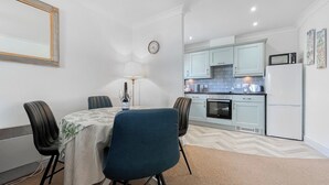 A compact kitchen with modern appliances, a dining area with a table and chairs, and a clock on the wall. - Abbey Lights - UK51880 (Whitby)