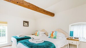 Un dormitorio con dos camas, una viga de techo de madera, una mesita de noche con lámpara y una ventana con cortinas.