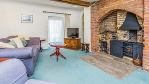 Una sala de estar con chimenea de ladrillo, un sofá, un televisor y una mesa de madera.