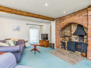 Ein Wohnzimmer mit Kamin aus Backstein, einer Couch, einem Fernseher und einem Holztisch.