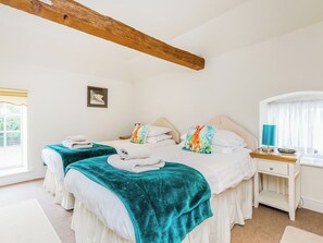 Ein Schlafzimmer mit zwei Betten, einem Holzbalken an der Decke, einem Nachttisch mit Lampe und einem Fenster mit Vorhängen.