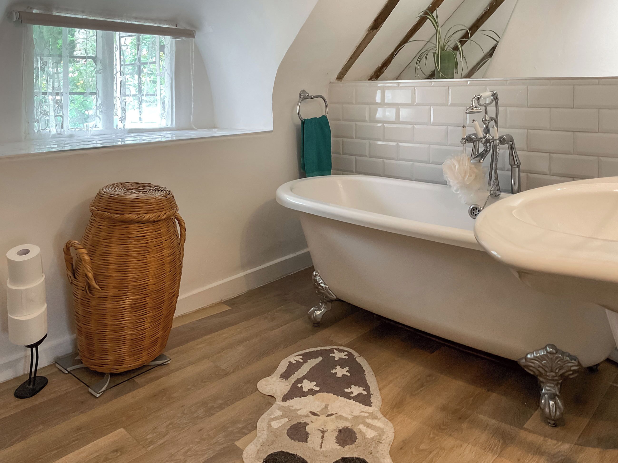 Een badkamer met een vrijstaand bad, toilet, rieten mand en een kamerbreed tapijt met dessin.