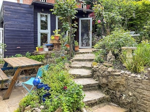 A garden with a wooden table and chairs, a stone staircase, and a variety of plants. - 2 bedroom accommodation in Barrington, near Ilminster, (Barrington, near Ilminster,)