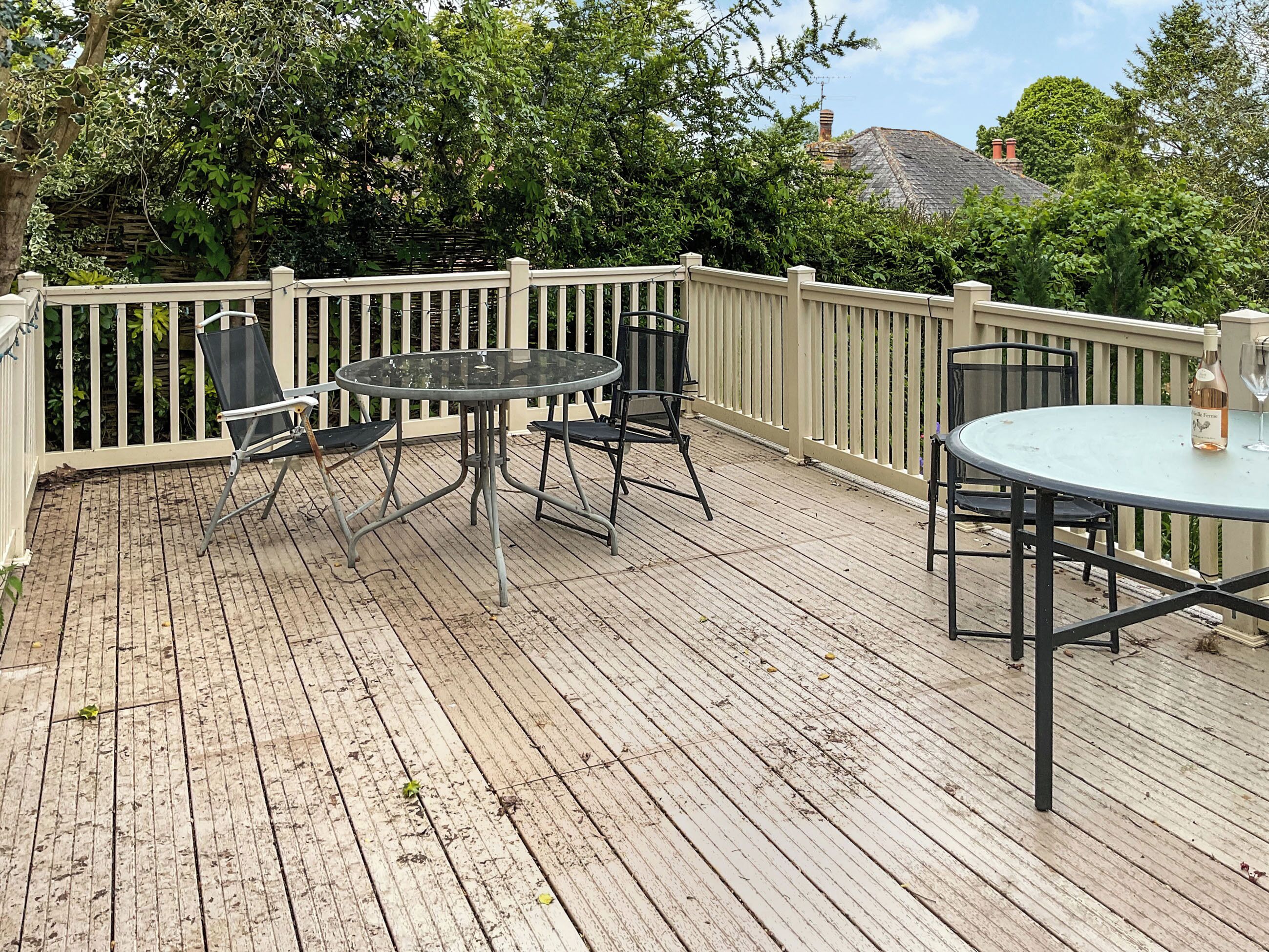 A wooden deck with a round table and chairs, surrounded by a white fence.