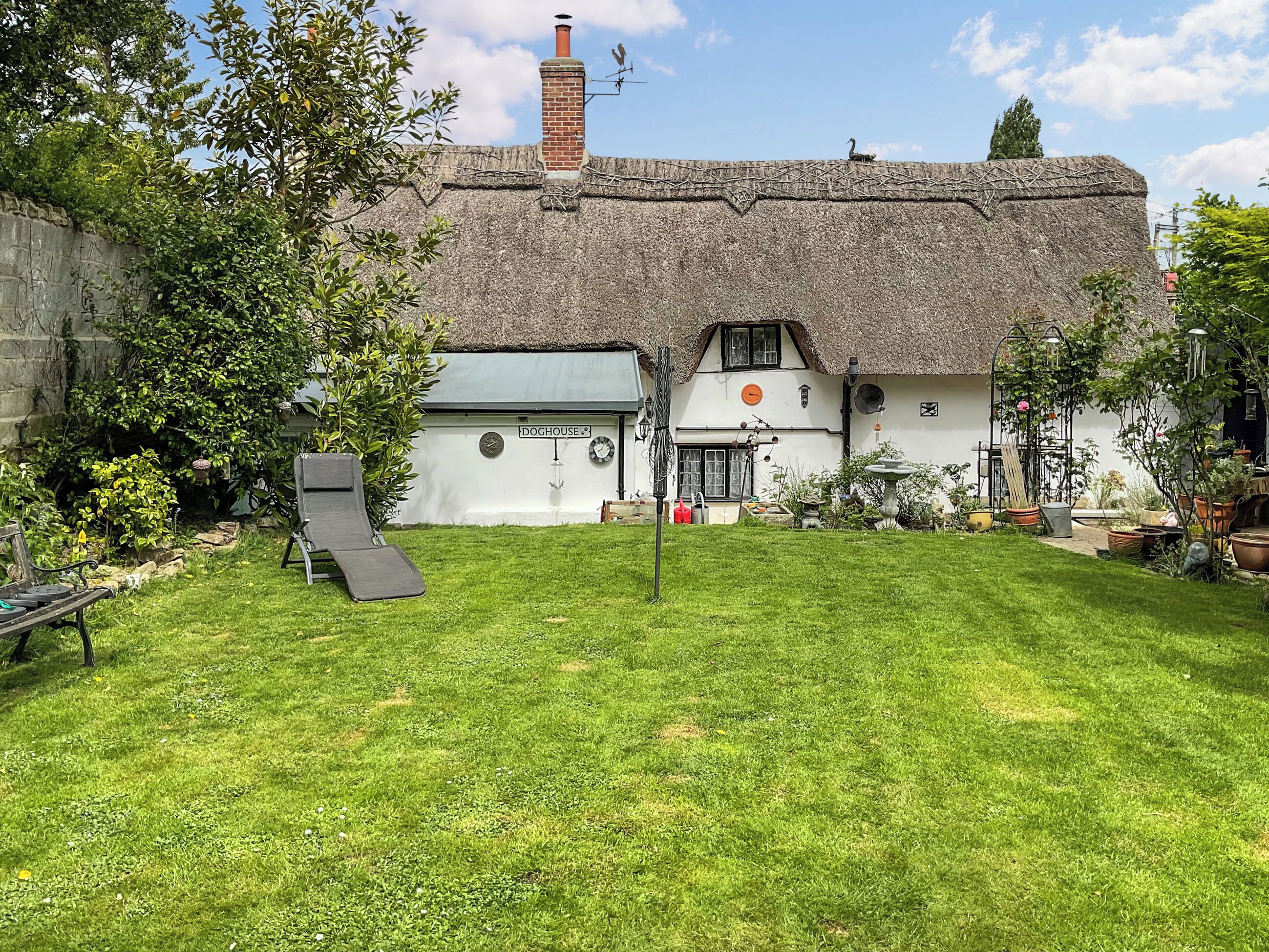 A thatched-roof house with a garden and a doghouse.