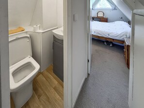 Una stanza compatta con servizi igienici, lavandino e letto, con un piccolo finestrino e una cassettiera in legno.
