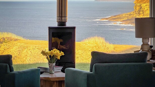 Een kamer met uitzicht op de oceaan, een open haard en een tafel met een bloevas.