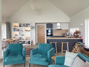 A spacious living area with teal armchairs, a wooden dining table, and a kitchen with modern appliances.