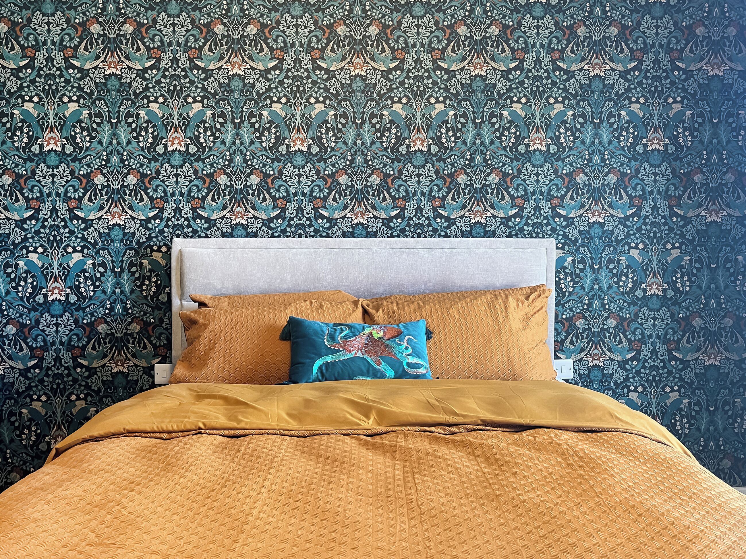 Una cama con cabecera, un papel tapiz estampado y una almohada decorativa.