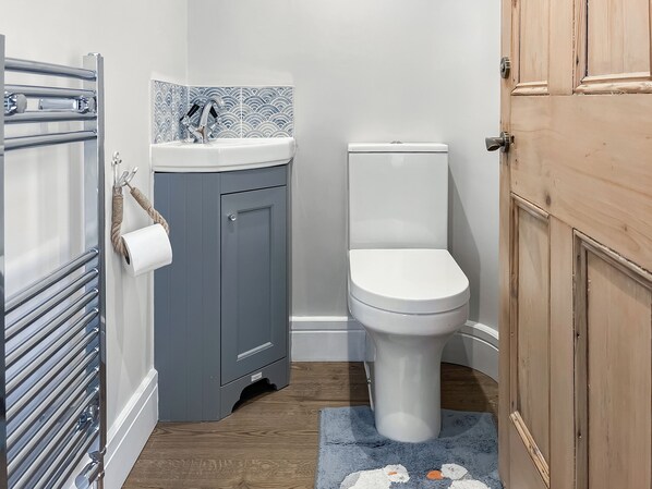 A bathroom with a toilet, a sink, a towel rack, and a wooden door. - 2 bedroom accommodation in Newbiggin-by-the-sea (Newbiggin-by-the-sea)