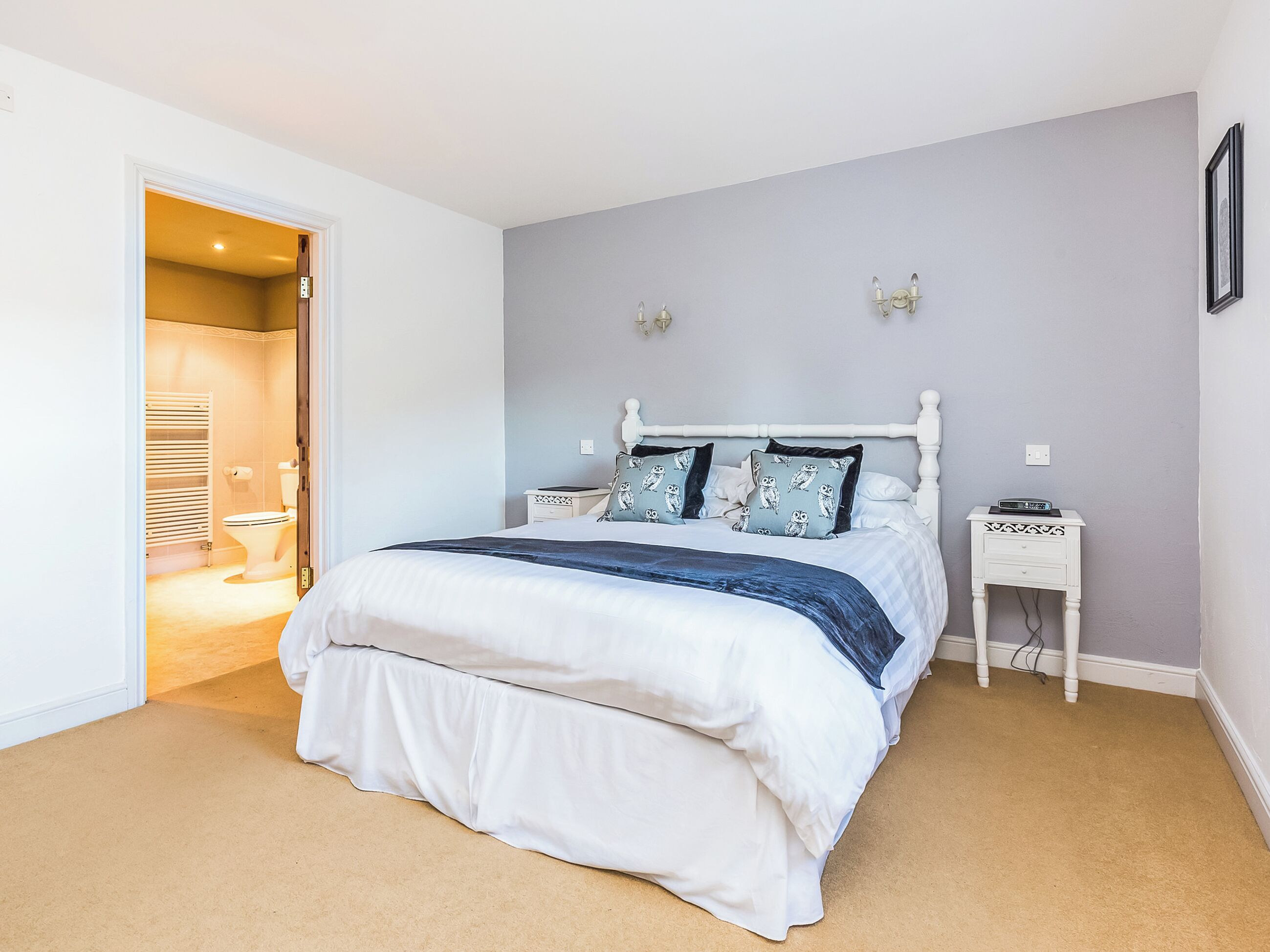 A bedroom with a bed, a nightstand, a wall-mounted lamp, and a door leading to a bathroom.