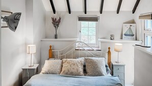 A bedroom with a bed, bedside tables, a window, a wall-mounted shelf, and a ceiling with exposed beams. - A cute cottage for two, set peacefully with regular red squirrel visitors. (Llaneilian, near Amlwch)