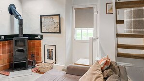 A cozy living room with a fireplace, a sofa, a window, and a framed map on the wall. - A cute cottage for two, set peacefully with regular red squirrel visitors. (Llaneilian, near Amlwch)