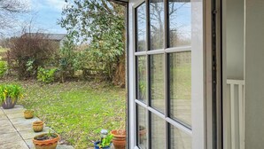 A view through a glass door into a garden with potted plants and a grassy area. - A cute cottage for two, set peacefully with regular red squirrel visitors. (Llaneilian, near Amlwch)