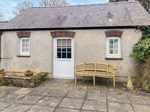 A traditional stone building with a white door, two windows, and a wooden bench outside.
