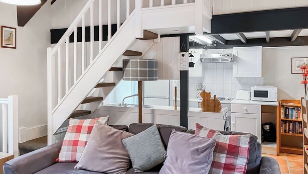 A living room with a grey sofa, a staircase, a kitchen area, and a bookshelf. - A cute cottage for two, set peacefully with regular red squirrel visitors. (Llaneilian, near Amlwch)
