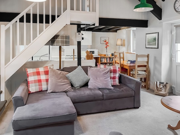 A modern living room with a grey sectional sofa, a wooden dining table, and a staircase.