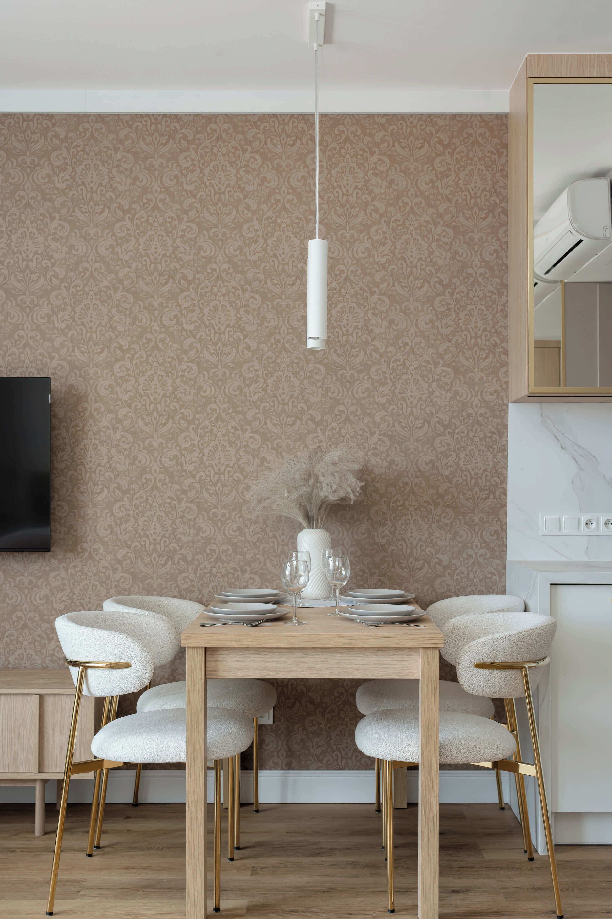 Un coin repas avec une table en bois, des chaises blanches, un vase contenant des fleurs séchées et un téléviseur fixé au mur.