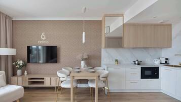 Una sala moderna con televisor de pantalla plana, una mesa de comedor con sillas, un sofá y una cocina con armarios y electrodomésticos.