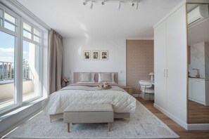 A bedroom with a large bed, a bedside table, a chair, and a view of the city through large windows.