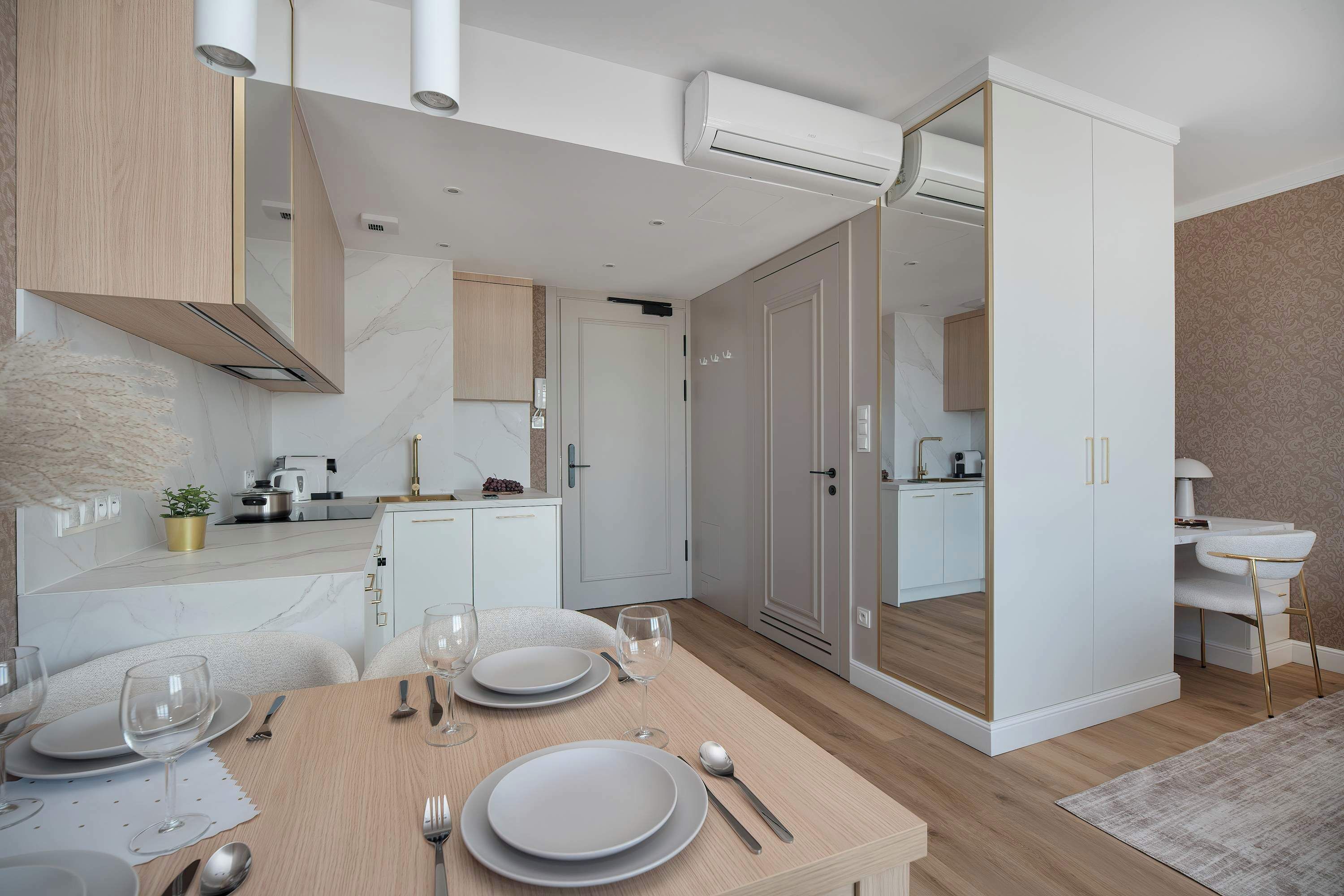 A modern kitchen with white cabinetry, a dining area with a wooden table set for four, and a mirrored closet door.