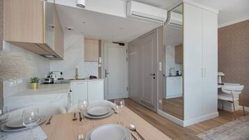 A modern kitchen with white cabinetry, a dining area with a wooden table set for four, and a mirrored closet door.
