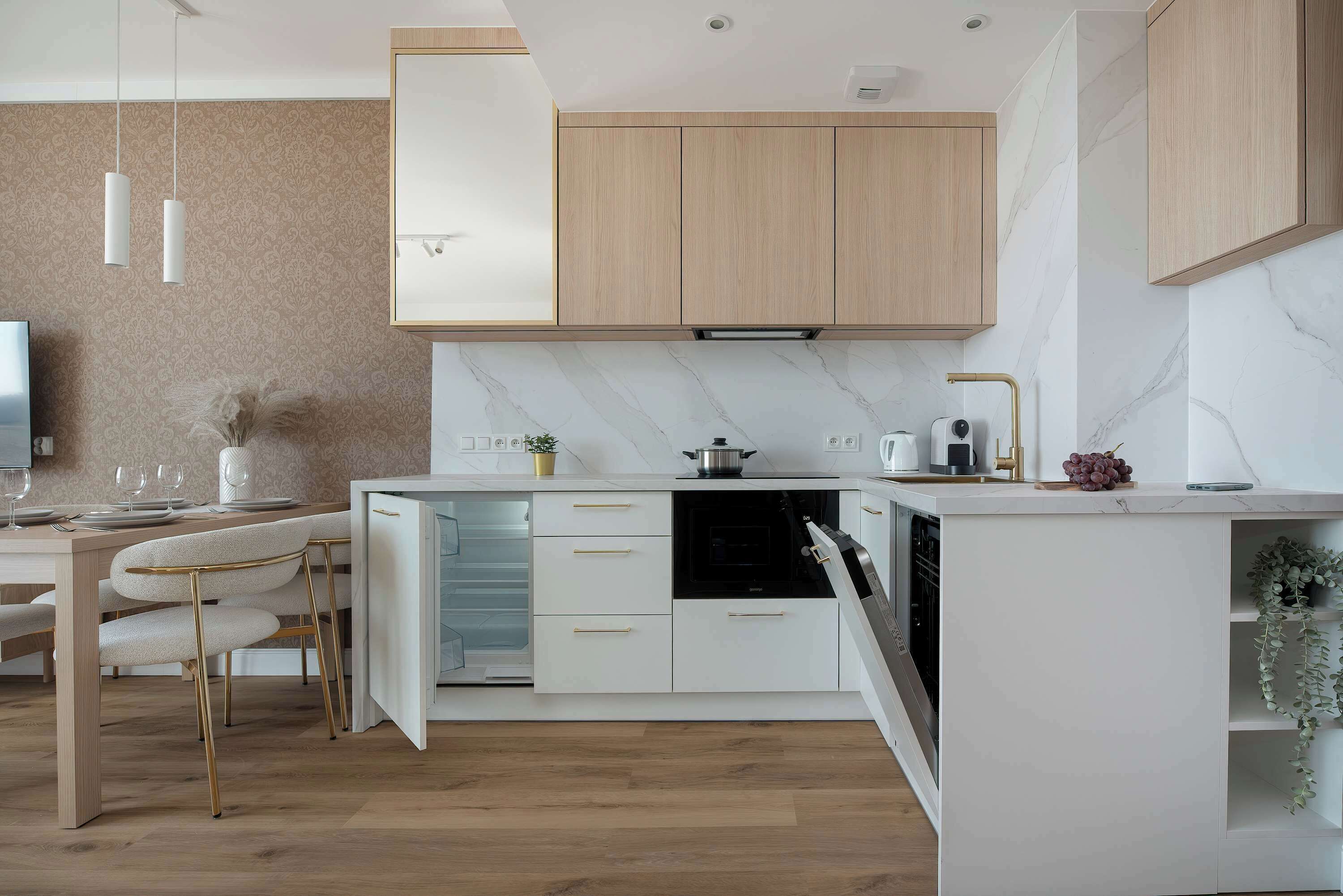 Una cocina moderna con horno empotrado, armarios blancos y un comedor con mesa y sillas.