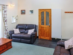 A living room with a leather sofa, a wooden door, and a whiteboard on the wall. - 3 bedroom accommodation in Llandello (Llandello)