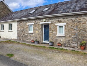 A stone building with a blue door, white-framed windows, and potted plants on the ground. - 3 bedroom accommodation in Llandello (Llandello)