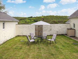 A patio with a table and chairs, a wooden door, and a white wall. - 3 bedroom accommodation in Llandello (Llandello)