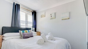 Un letto ben rifatto con lenzuola bianche, una testiera e un comodino con una lampada.