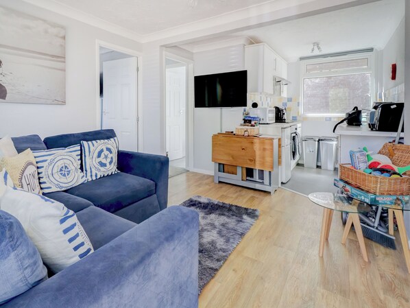 Una sala de estar moderna con un sofá azul, una mesita de madera y una cocina con electrodomésticos.