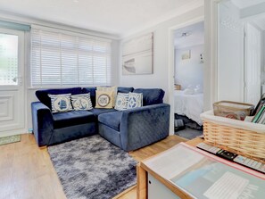 Una sala de estar acogedora con un sofá azul, un felpudo gris y una pequeña mesa de madera con una cesta.